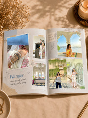 An open custom photo album spread on a beige fabric surface, surrounded by dried flowers, a lit candle, and a bowl of jewelry. The pages feature printed layouts with embedded photos of women in traditional and casual outfits, scenic backgrounds, and decorative text including 'Wander'.